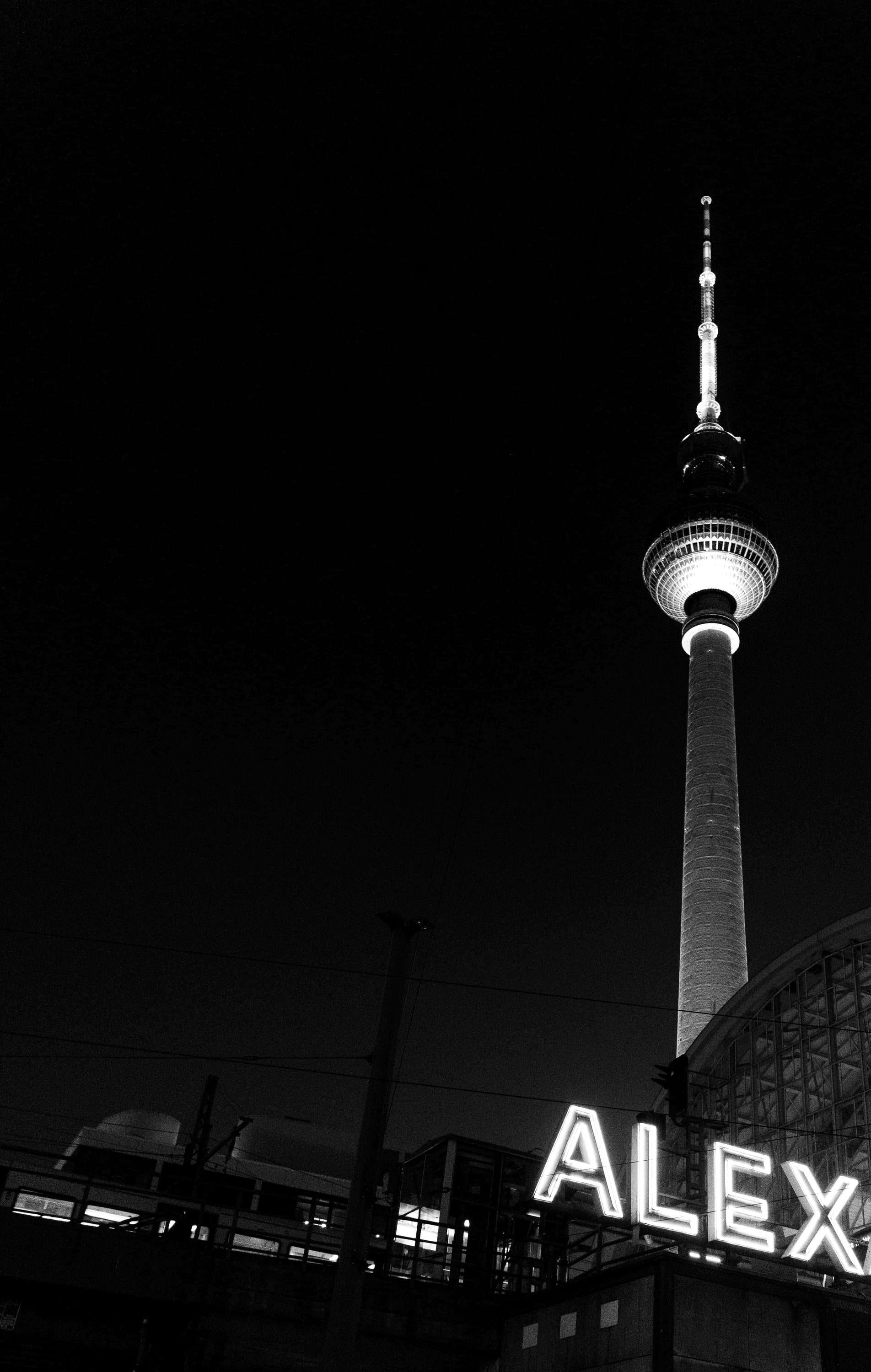 The Berlin TV tower lit against a black night sky, with the illuminated ALEX sign below.