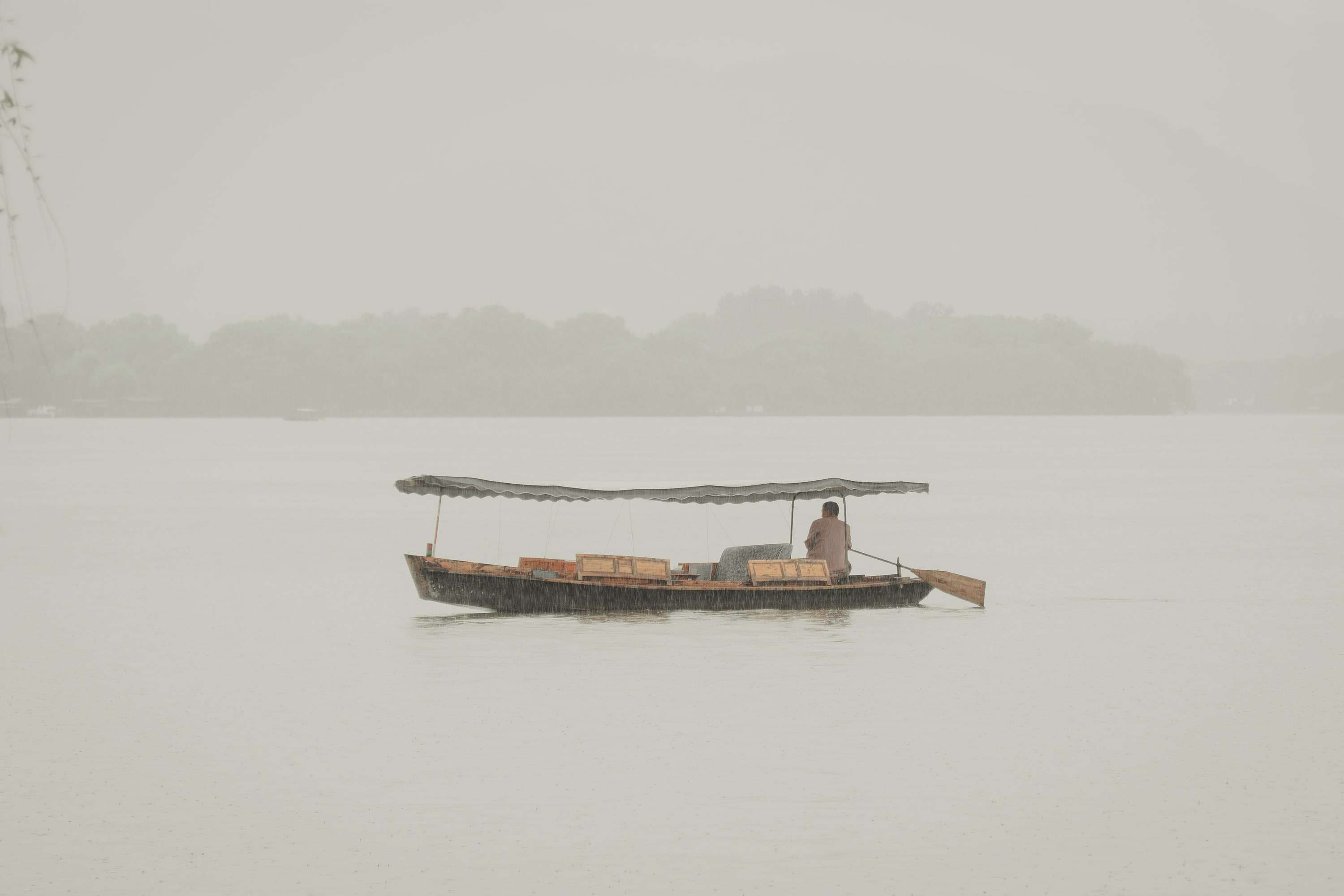 A single covered wooden boat on flat, misty water with a faint tree line behind.