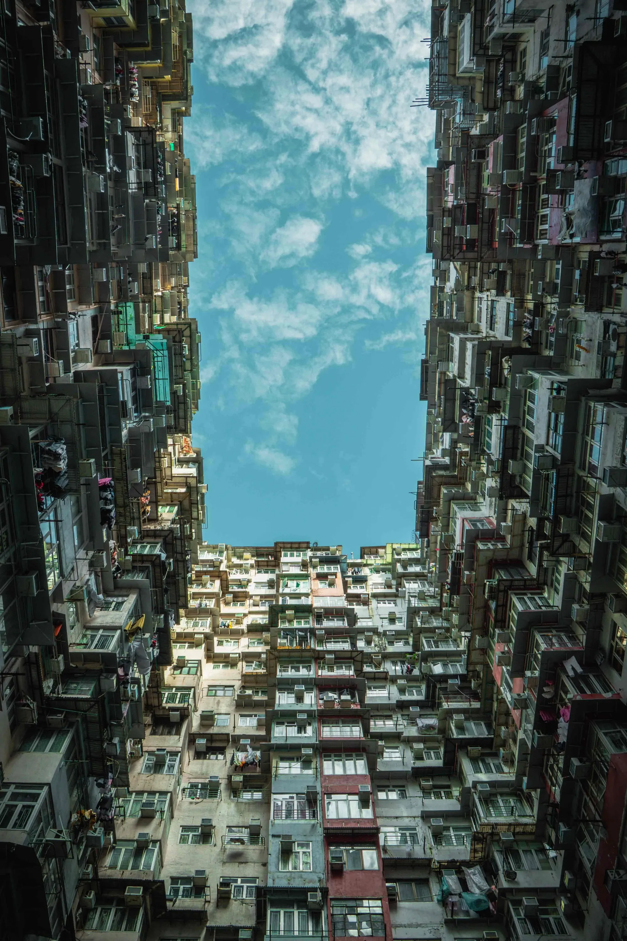 Looking straight up between the stacked apartment blocks of the Yik Cheong Building towards a strip of sky.